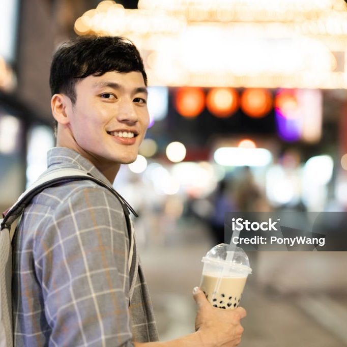 back view of asian man takes a cup of tapioca ball tea at night market while on vacation in Taiwan